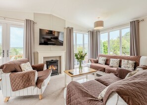 A modern living room with a fireplace, a flat-screen TV, and large windows offering a view of the outdoors. - 3 bedroom accommodation in Bala, (Bala,)