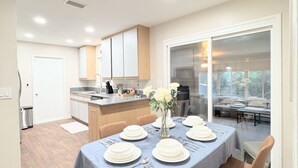 Una cucina moderna con mobili bianchi, un'area pranzo con tavolo imbandito per quattro persone e un'ampia finestra con vista sull'esterno.