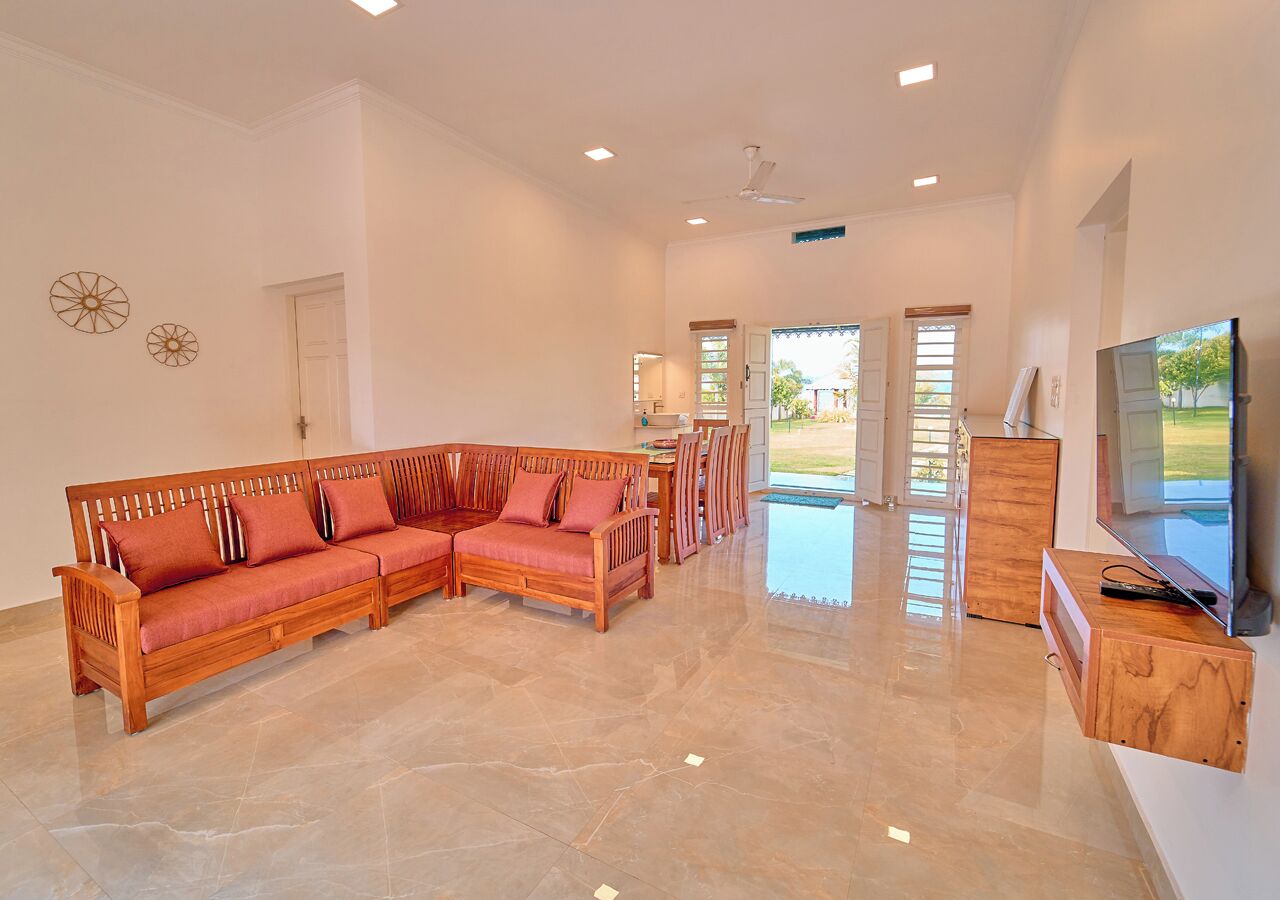 Amplia sala de estar con un sofá de madera en forma de L, un mueble bajo para televisión de madera y un comedor con mesa y sillas.