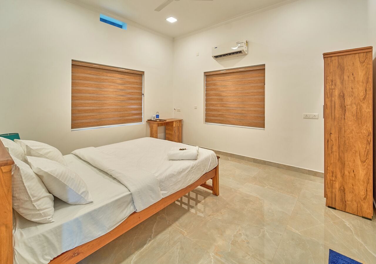 A bedroom with a bed, wooden wardrobe, and an air conditioning unit on the wall.