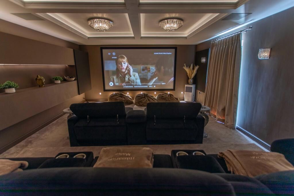 A home theater with a large screen, comfortable seating, and a ceiling with chandeliers.