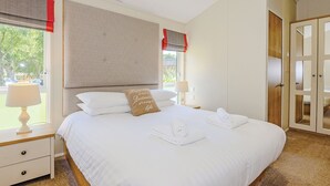 Une chambre d’hôtel avec un grand lit, deux tables de chevet, une fenêtre avec des rideaux, une porte et une vue sur les arbres à l’extérieur.