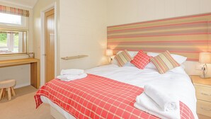 Quarto de hotel com cama, luminárias de cabeceira, janela com cortinas, escrivaninha de madeira e prateleira fixada na parede.