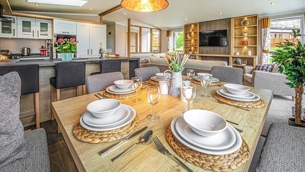Una cocina moderna con armarios blancos, un comedor con mesa de madera dispuesta para seis personas y un televisor en la sala de estar.