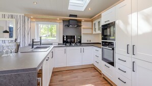 Cocina moderna con armarios blancos, una isla central, tragaluces y vistas al exterior.