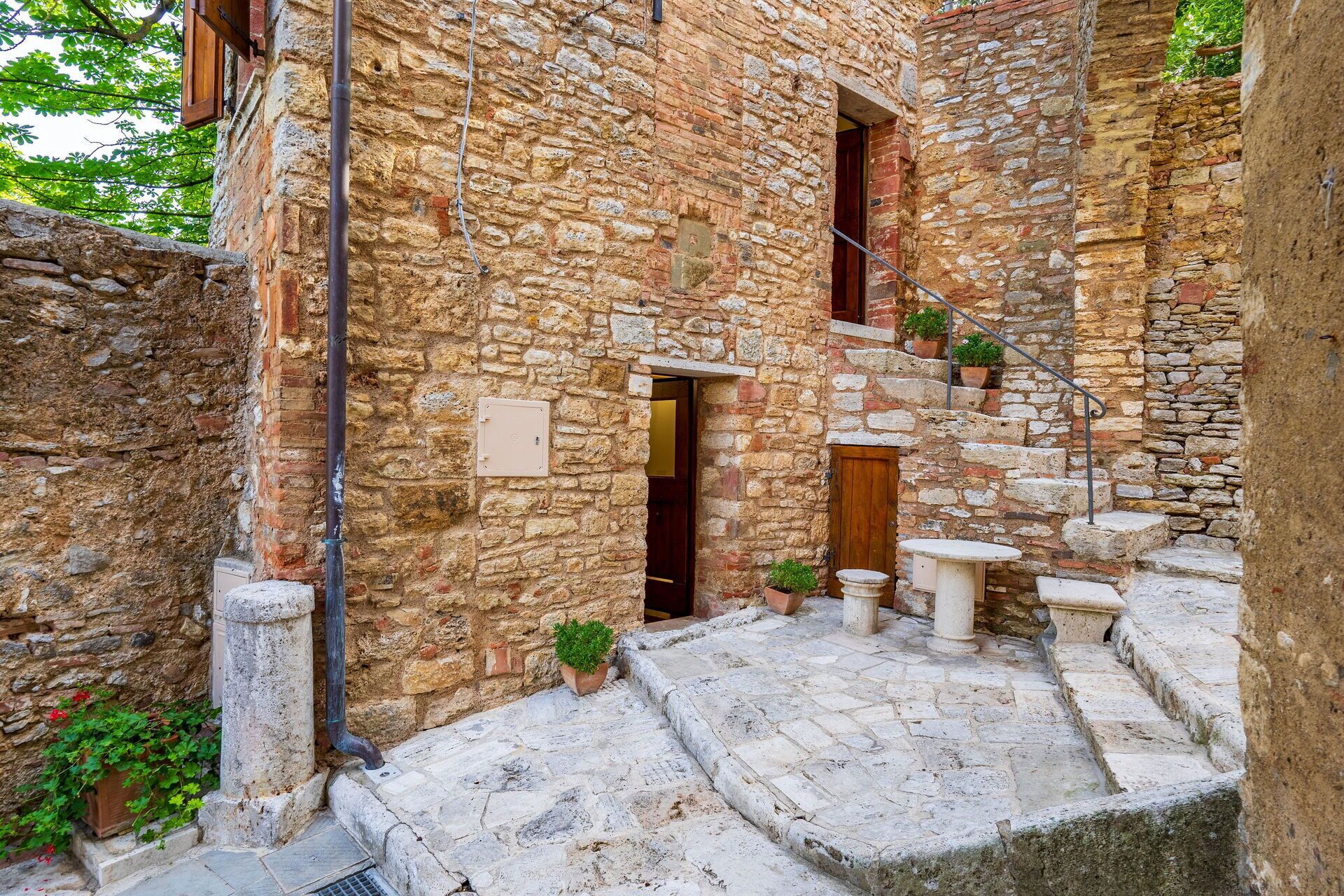 A stone building with a narrow staircase leading to a door. There are potted plants on the steps and a small table at the bottom.