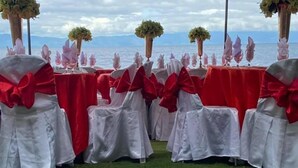 Une décoration de mariage avec des tables recouvertes de nappes rouges et blanches, agrémentées de grands nœuds rouges, et entourées de chaises dotées de jupes blanches et de nœuds rouges.