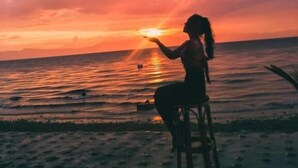 La silhouette d’une personne assise sur une chaise, face à l’océan, au coucher du soleil.