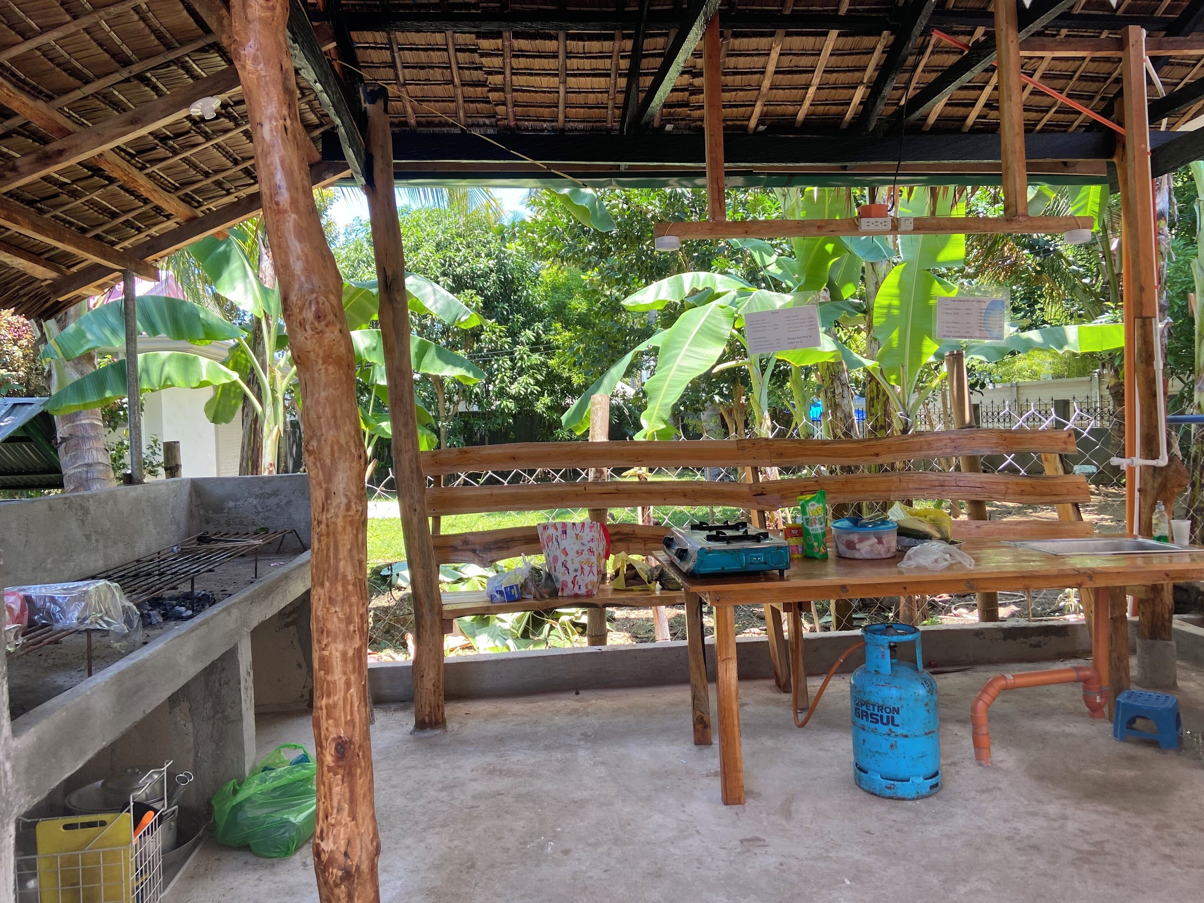 Un espace cuisine extérieur de style rustique, doté d’un plan de travail en béton, d’une cuisinière à gaz et d’une bouteille de gaz bleue.