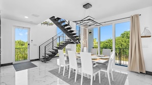 A modern dining area with a black spiral staircase, a chandelier, and a large window with a view of greenery. - Copa D Oro 835 in Marathon (Marathon)