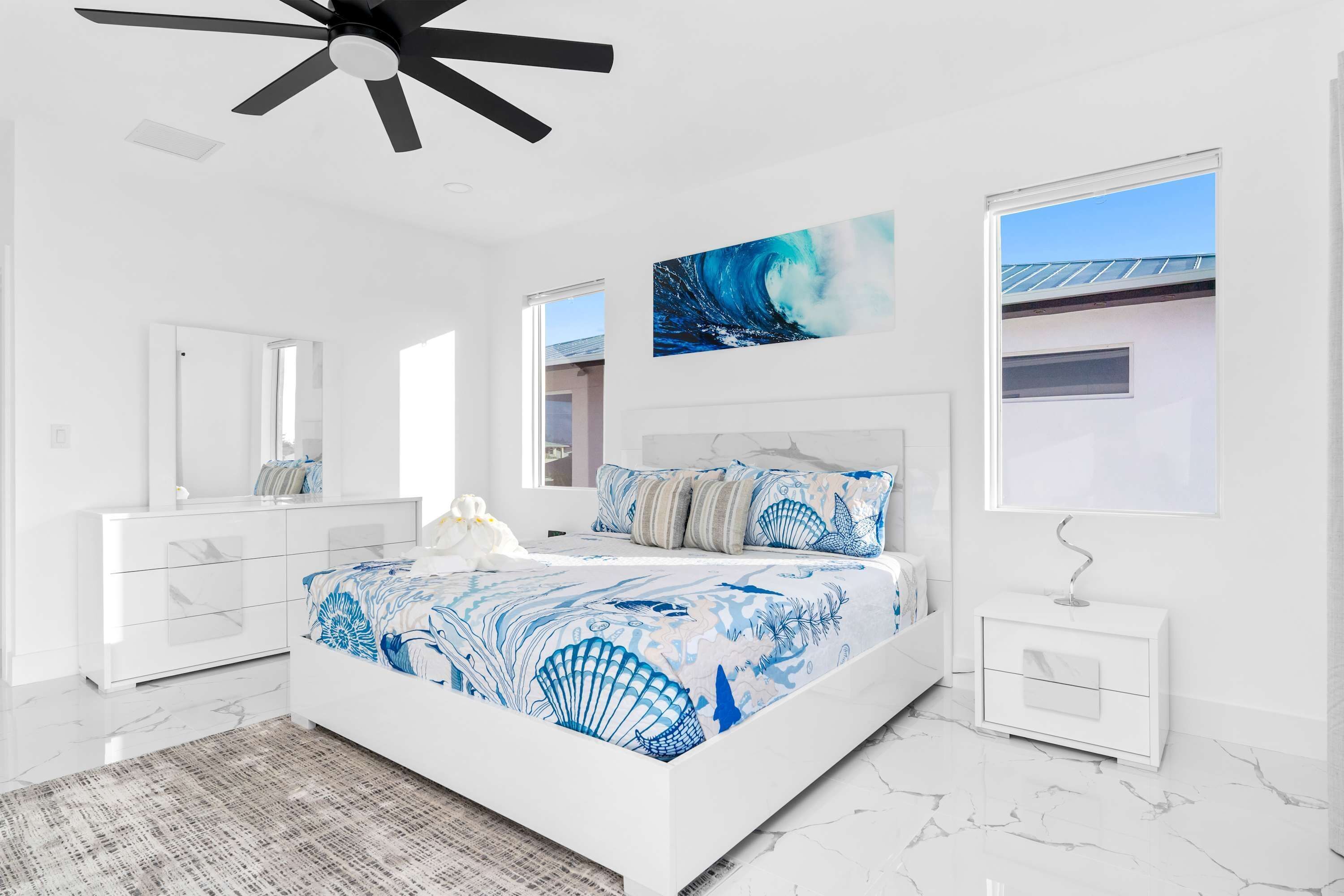 A modern bedroom with a large bed, a ceiling fan, a view of the outside, and a bathroom with a sink and mirror.