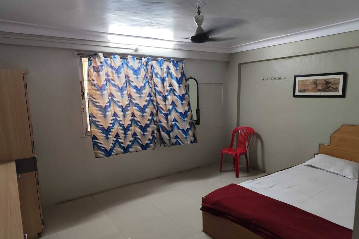 A bedroom with a bed, a red chair, a ceiling fan, and a patterned curtain.