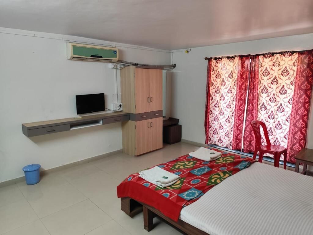 Un dormitorio con cama, televisor, armario y ventana con cortinas.
