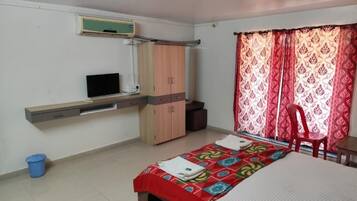 Un dormitorio con cama, televisor, armario y ventana con cortinas.