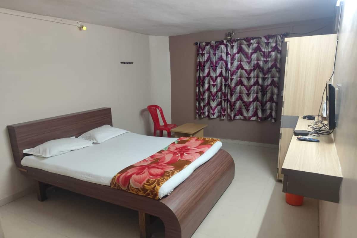 A hotel room with a wooden bed, a red chair, a desk, a TV, and patterned curtains.