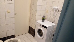 Et lille badeværelse med vaskemaskine, toilet og en lille plantepotte.