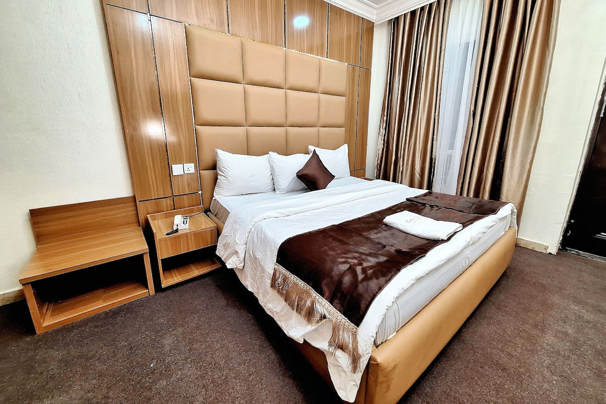 Ein ordentlich eingerichtetes Hotelzimmer mit einem großen Bett, einem Nachttisch und einer Bank.