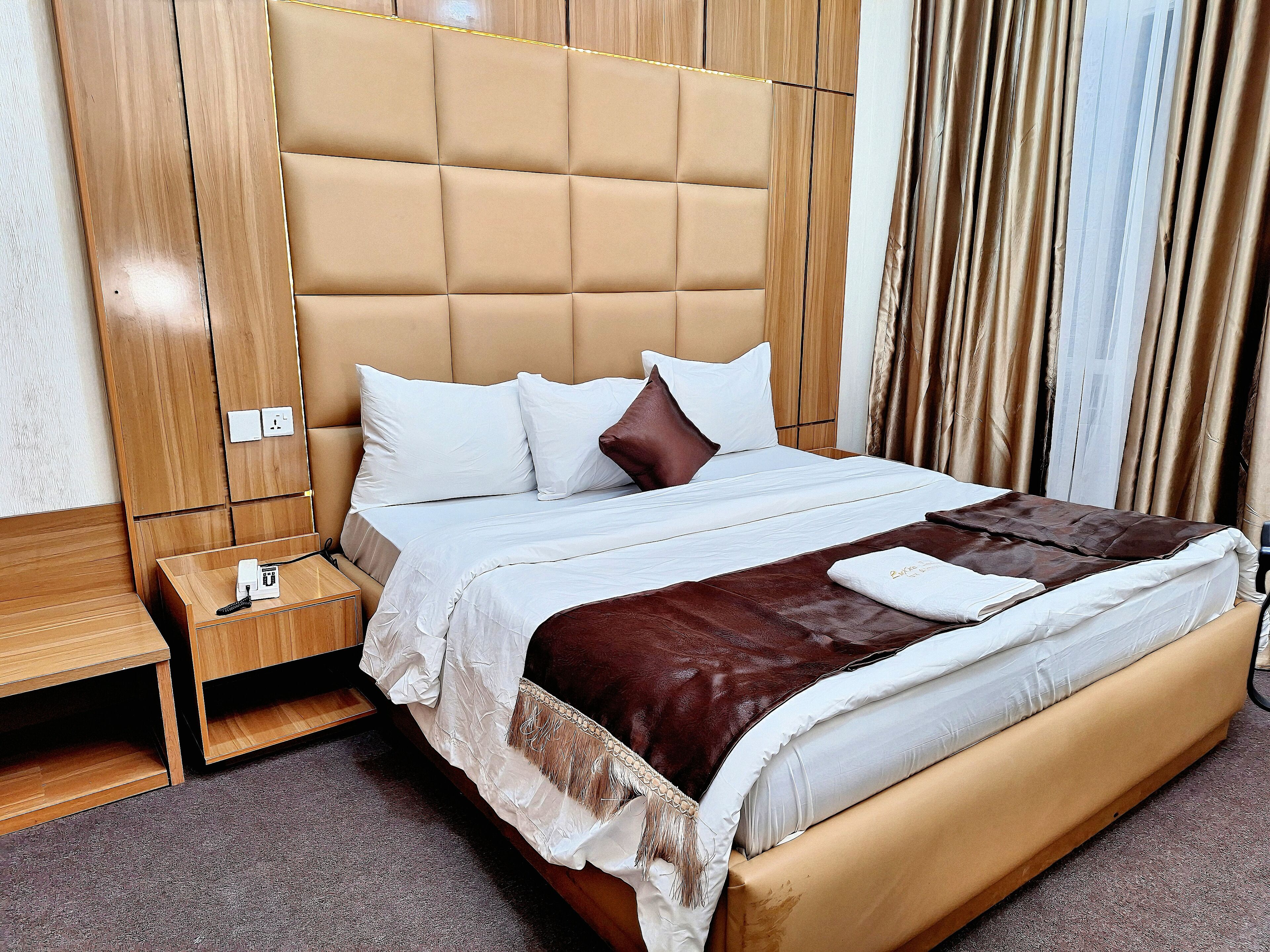 A hotel room with a large bed, a bedside table with a phone, and a power outlet.