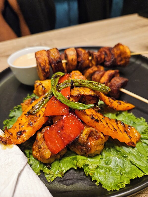 Un plato de verduras a la parrilla y brochetas de carne, acompañado de salsa para mojar.