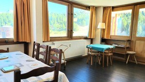 Ein Zimmer mit Esstisch, Stühlen, einem kleinen Tisch mit Tischdecke und einem Heizkörper.
