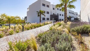 A modern building with a paved pathway and landscaped garden with various plants and a palm tree. - Beautiful new build apartment Estepona - Estepona, Andalucía (Estepona)