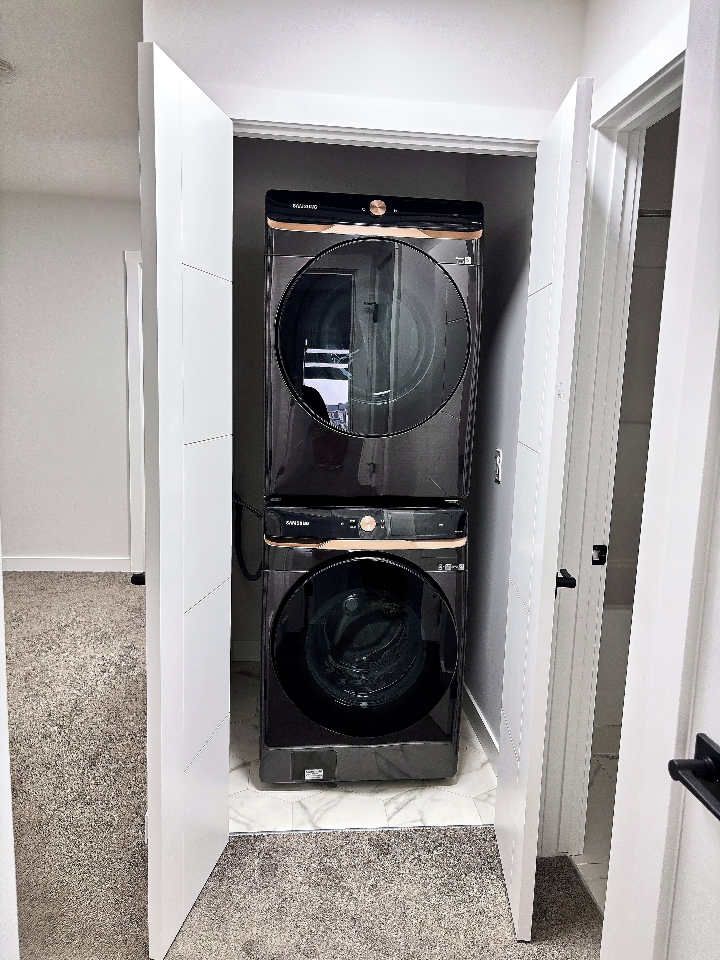 A compact laundry room with two black washing machines, a white door, and a grey carpet.