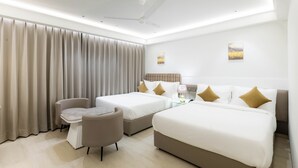 A modern hotel room with two beds, a sofa, a small table, and a ceiling fan. - Emerald Luxe A Boutique Hotel (Mohali)