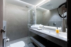 Un baño moderno con cabina de ducha de vidrio, un espejo grande y un tocador con perchero.