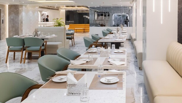 Ein modernes Restaurant mit Marmorböden, grünen Sitzstühlen und ordentlich gedeckten Tischen mit weißen Tischdecken und Besteck.