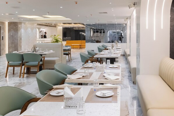 A modern restaurant with marble flooring, green upholstered chairs, and neatly arranged tables with white tablecloths and silverware. - Emerald Luxe A Boutique Hotel  (Mohali)