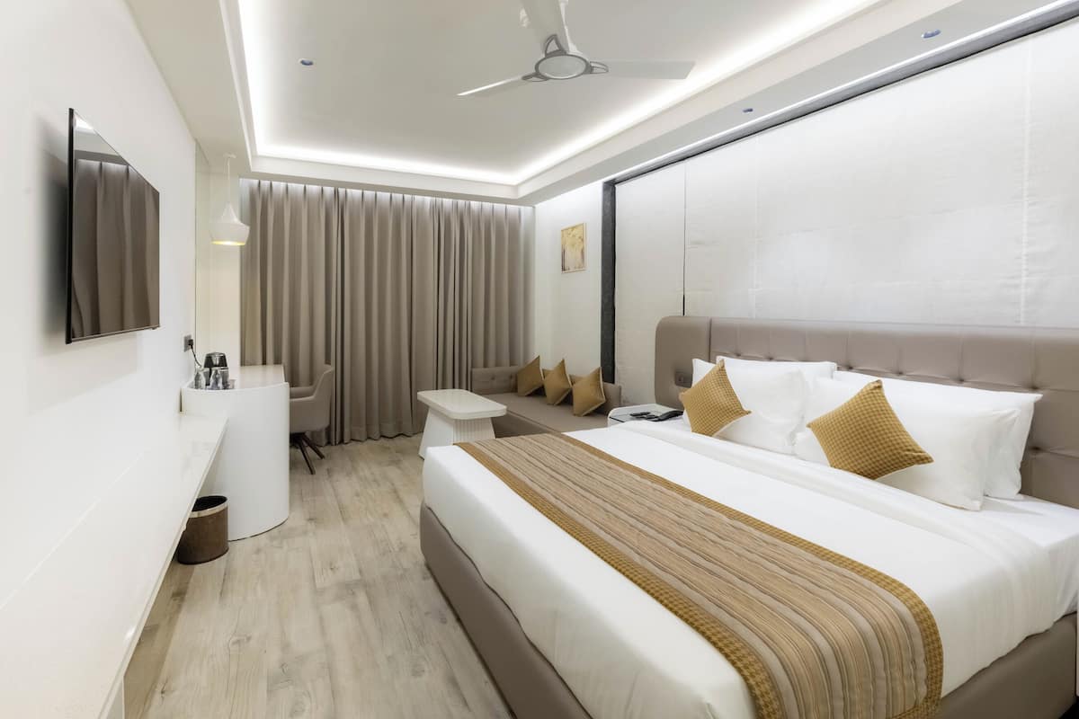 A modern hotel room with a large bed, a desk, a chair, a TV, and a ceiling fan.