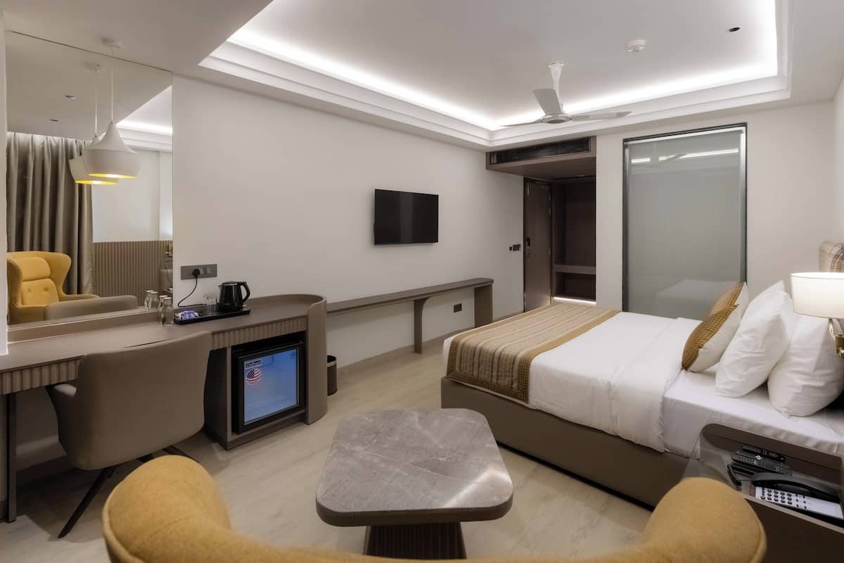 A modern hotel room with a bed, desk, chair, television, and a large mirror.