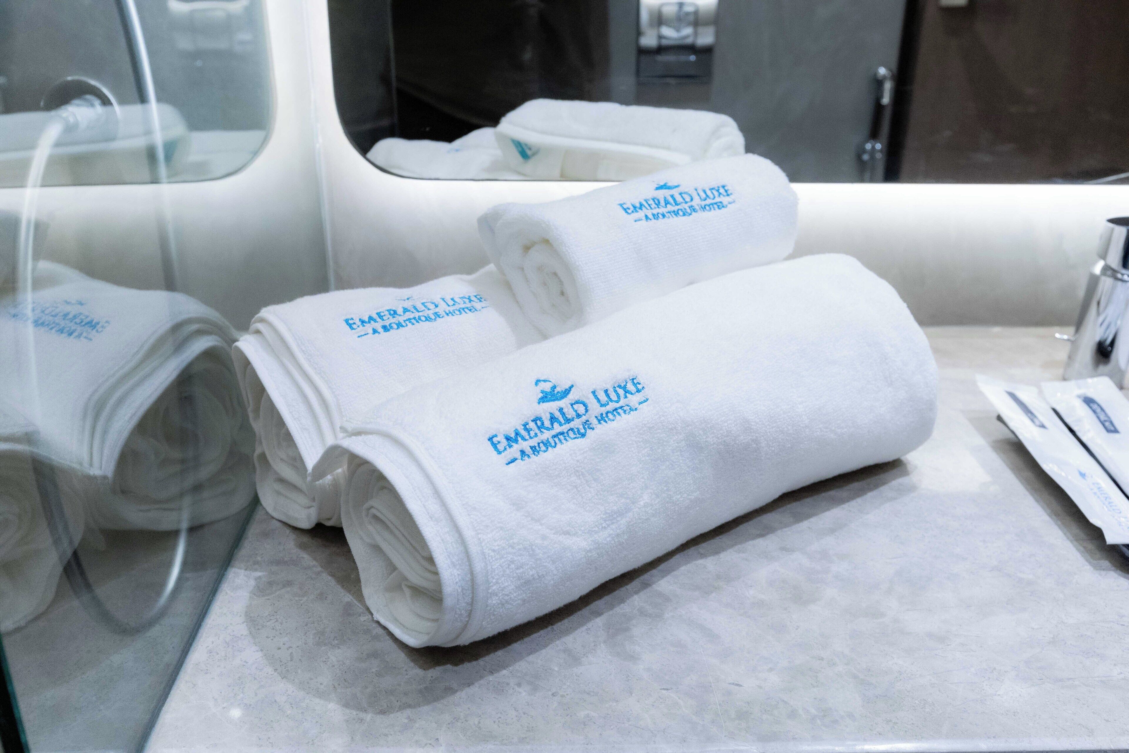 Toallas blancas dobladas con el logotipo de 'Emerald Luxe Boutique Hotel' sobre una encimera de mármol.