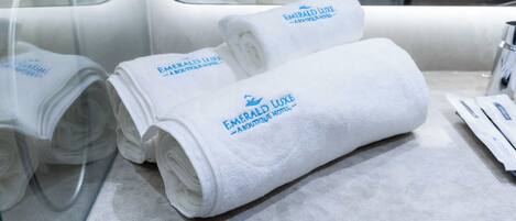 Neatly folded white towels with "Emerald Luxe Boutique Hotel" branding on a marble countertop.