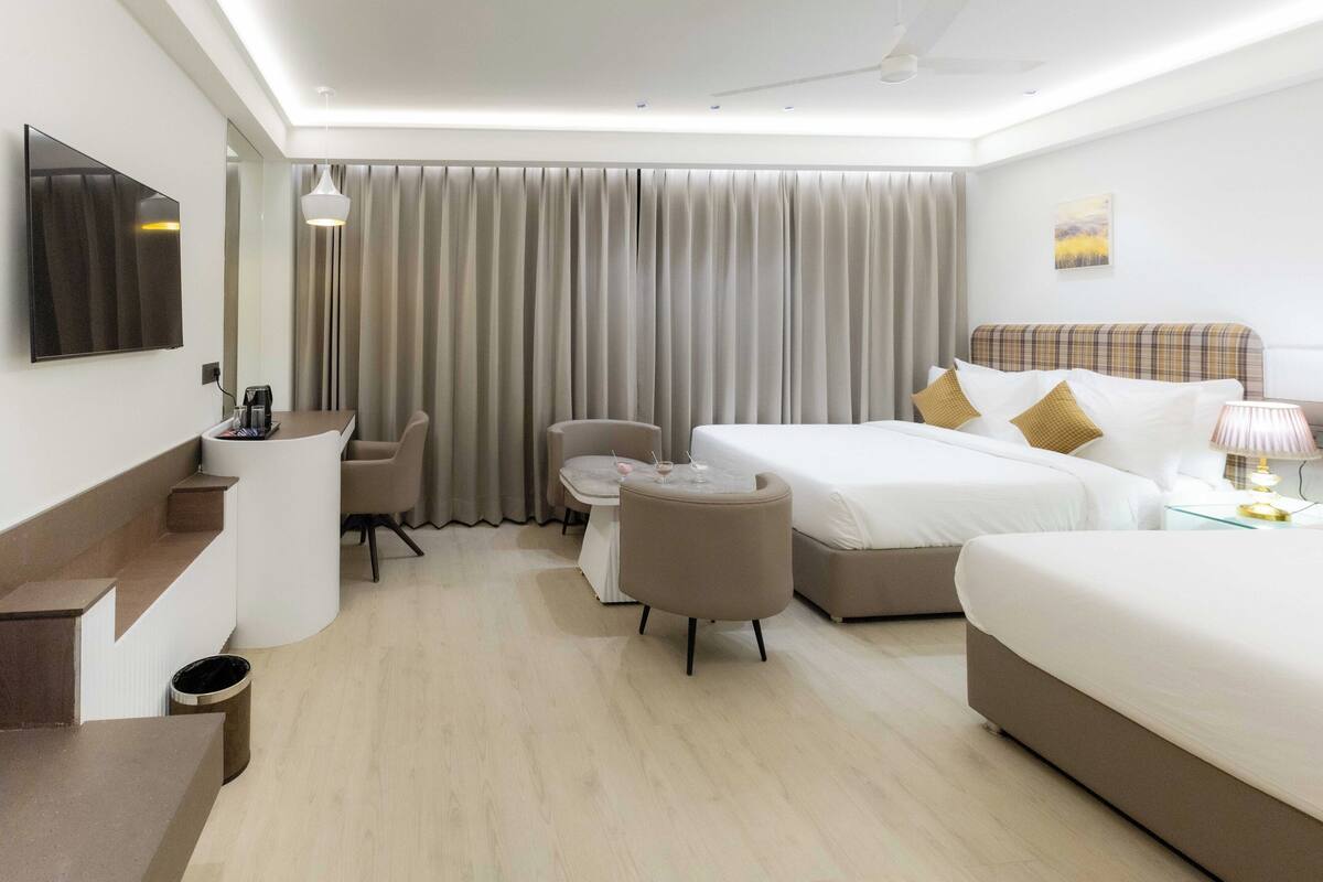 A hotel room with a bed, a desk with a chair, a sofa, a TV, and a window with curtains.