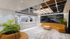 A modern lobby with a reception desk, a curved sofa, and a potted plant. - Emerald Luxe A Boutique Hotel (Mohali)