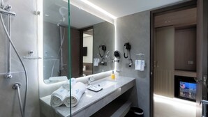 Een moderne badkamer met een glazen douchecabine, een grote spiegel, een wastafelmeubel en haardroger(s) bevestigd aan de muur.