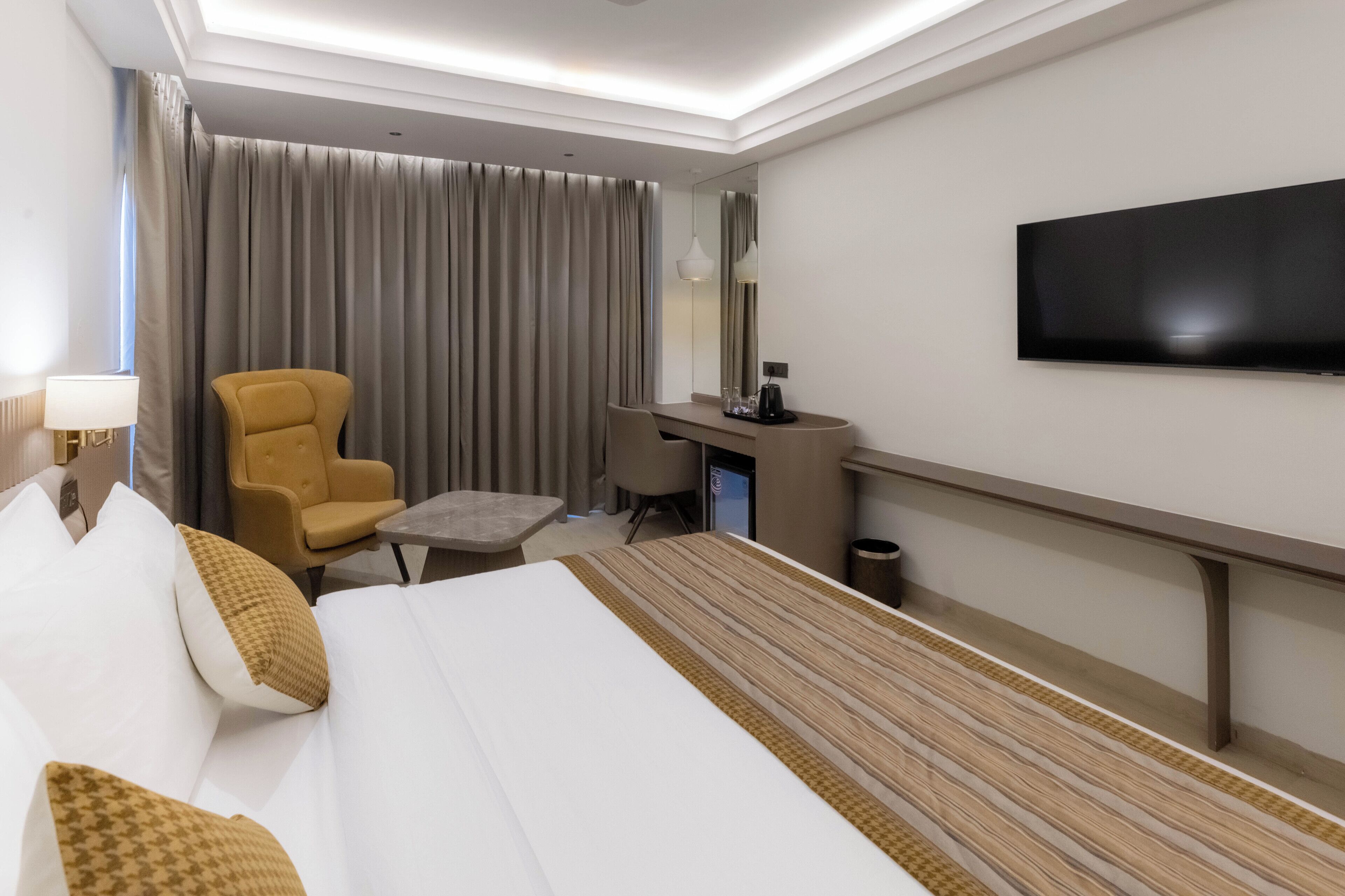Una habitación de hotel con cama, escritorio, silla, televisor y ventana con cortinas.