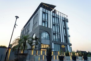 Un hôtel moderne, avec une entrée imposante, de grandes fenêtres et une enseigne indiquant qu’il s’agit de l’Emerald Luxe Boutique Hotel.