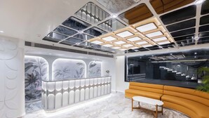 A modern interior with a marble floor, a curved sofa, a reception desk, and a ceiling with a geometric pattern. - Emerald Luxe A Boutique Hotel (Mohali)