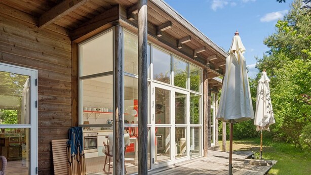 Eine Holzhütte mit großen Glasfenstern, einer Terrasse und Sonnenschirmen.