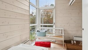 Ein Schlafzimmer mit großem Fenster, einem Bett, einer weißen Bank und einem Korbwägelchen.