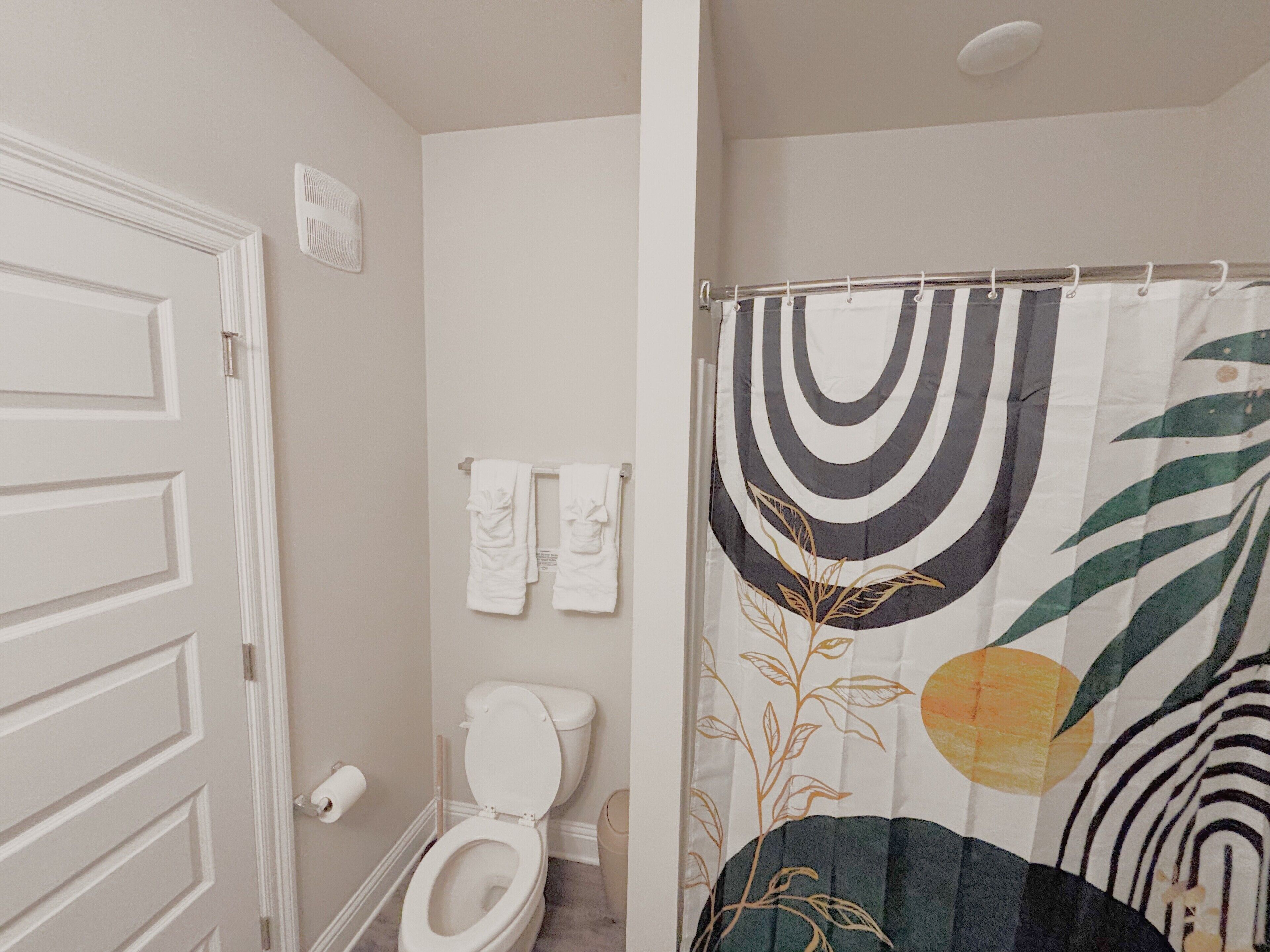 Un baño con inodoro, toallero y cortina de ducha con estampado de hojas.