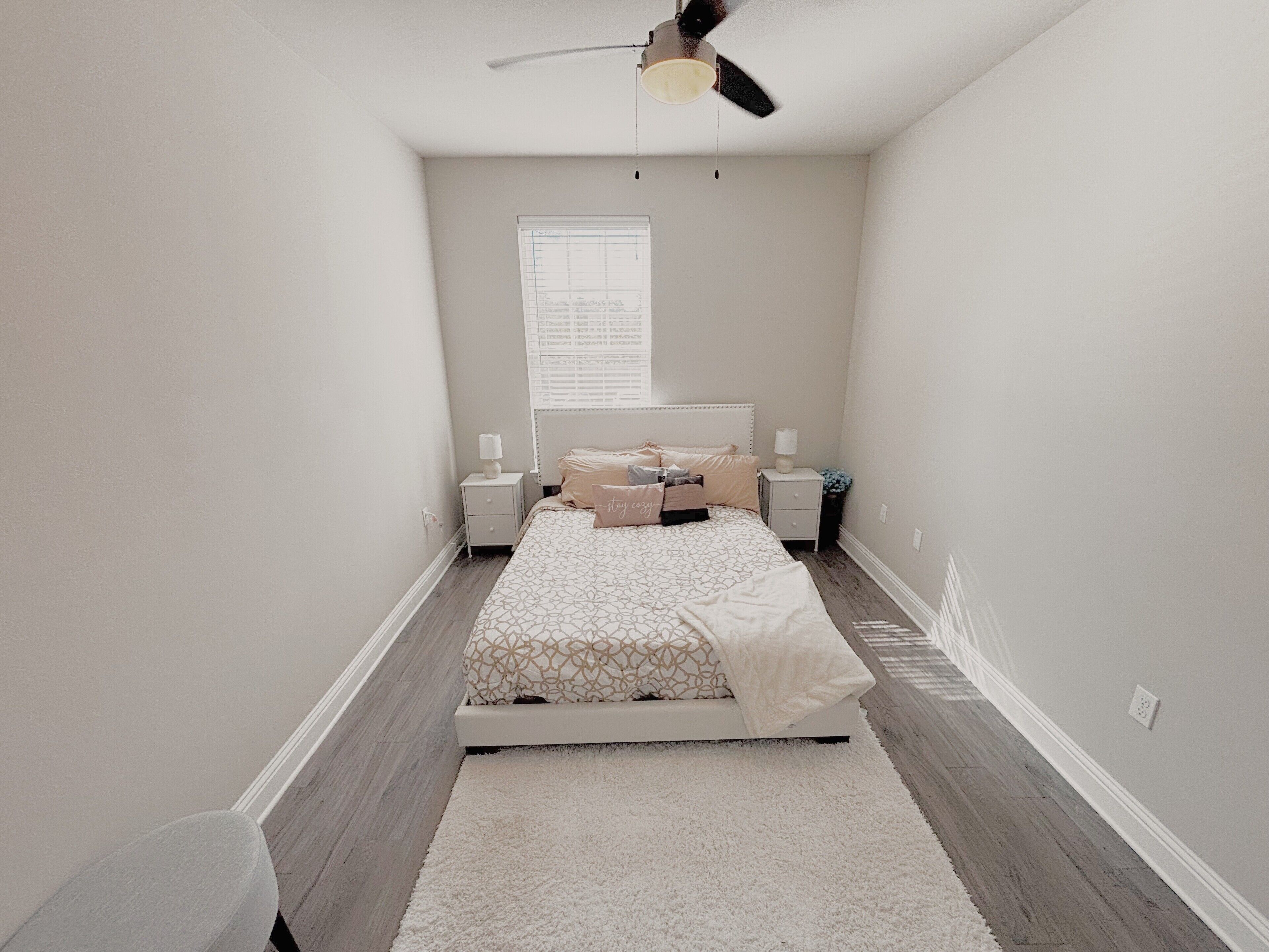 A bedroom with a bed, bedside tables, a ceiling fan, and a window.