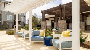 Een buitenzitplaats met een witte pergola en stenen zuilen, met blauw-witte banken en gele kussens.