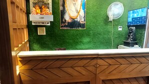 A reception desk with a green wall, a wooden counter, and a fan. - Hotel Mukesh Palace (Prayagraj)