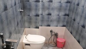 A compact bathroom with a white toilet, a pink bucket, and a small pink trash bin. - Hotel Mukesh Palace (Prayagraj)
