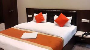 A neatly made bed with white and orange bedding, a dark headboard, and two orange pillows. - Hotel Mukesh Palace (Prayagraj)