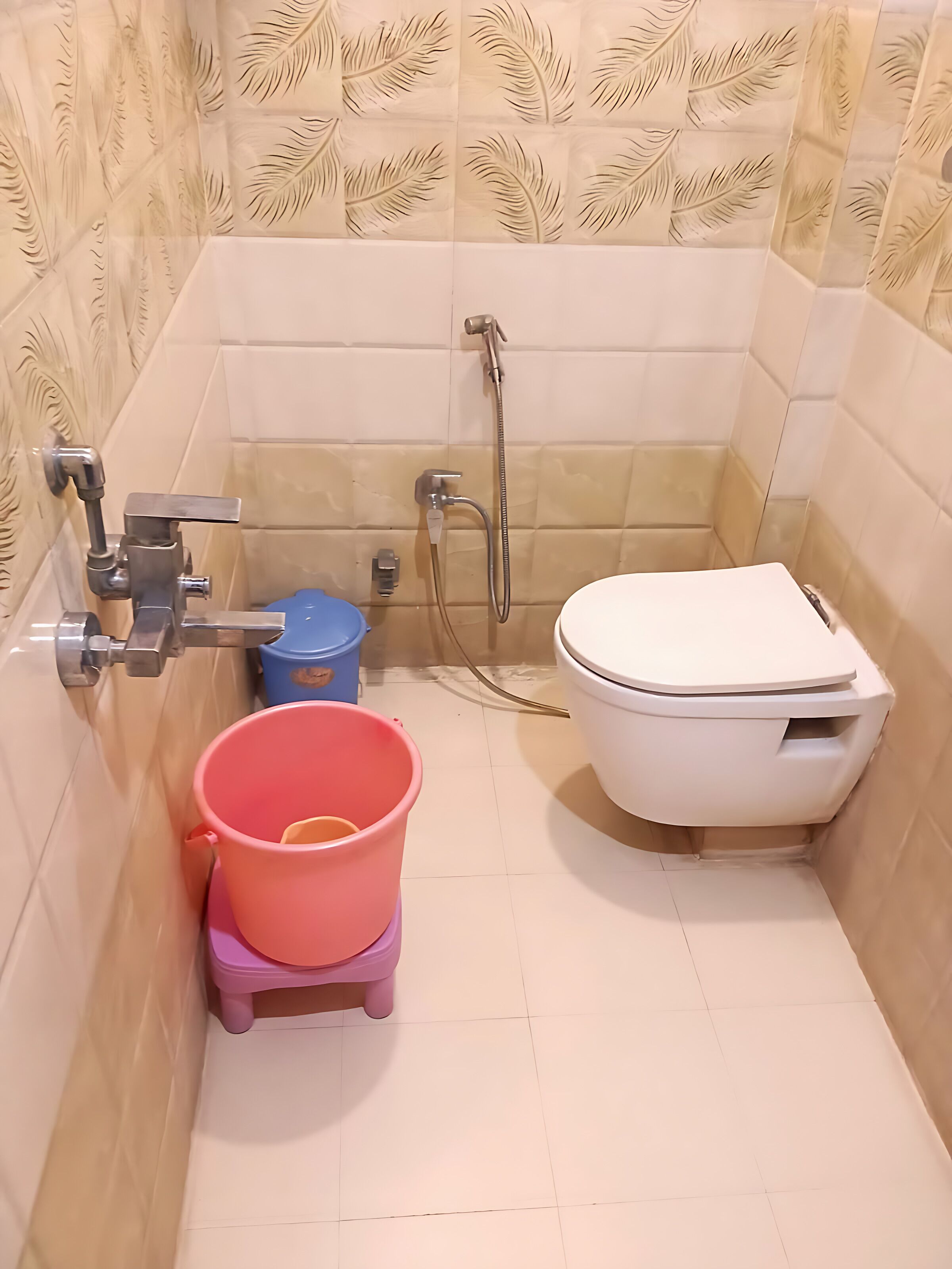 A small bathroom with a toilet, a shower, and a sink. There is a pink bucket and a blue trash bin.