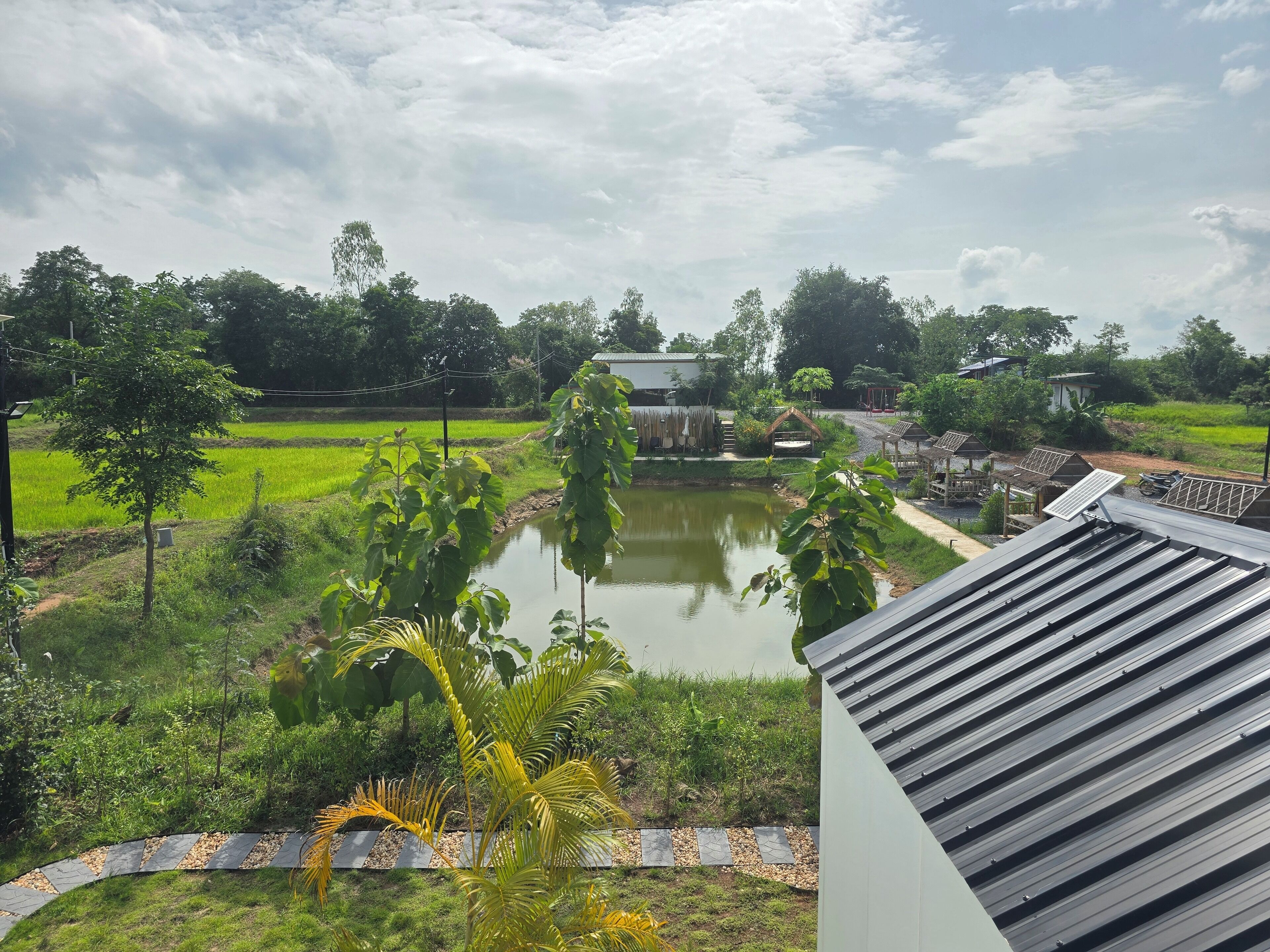 A view of a lush green landscape with a pond, trees, and a small bridge.